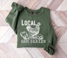 This funny Easter Egg Dealer Shirt is perfect for any Chicken or Egg lover! This Women Easter Tee is a unisex fit, so cute and soft great for lounging at home or going out on the farm or running errands. This funny Chicken Mom shirt is great to use as Matching Easter Shirts for your entire family! These shirts and easter sweatshirts also make perfect easter gifts for women! Enjoy our Happy Easter Shirt with your friends and loved ones this Easter day! { S H I R T / D E T A I L S } T-Shirts are 1 Couture, Country Fashion, Chicken Mom, Sweatshirt Details, Farmer Shirt, Chicken Shirts, Funny Chicken, Chicken Lady, Letter Print Sweatshirt