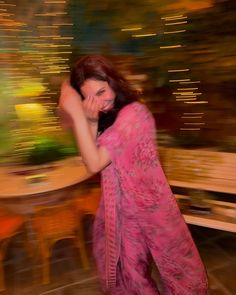 a woman in a pink sari is dancing with her hands behind her head and looking at the camera