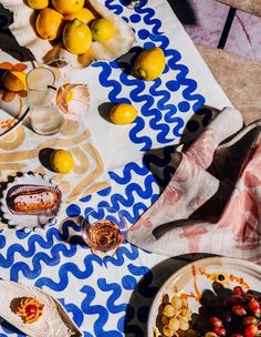 a table topped with plates of food next to lemons and other fruit on top of a blue and white cloth