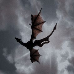 a black and white photo of a dragon flying through the air with clouds in the background