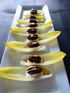 small appetizers are lined up on a long white platter with bananas and nuts