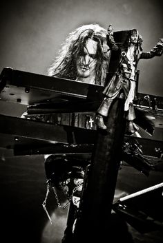 a man with long hair standing next to a piano