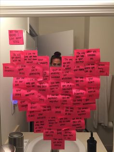 a woman is looking at her reflection in the mirror with sticky notes attached to it