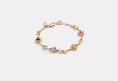 a gold bracelet with different colored stones and charms on the clasp, against a white background