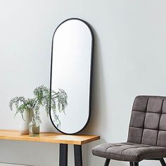 a mirror sitting on top of a wooden table next to a chair and potted plant
