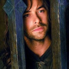 a man with long hair and blue eyes looking out from behind the bars in front of him