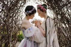 two women in dresses standing next to each other under a tree with no leaves on it