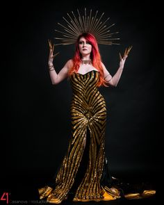 a woman with red hair wearing a gold dress and holding her hands up in the air