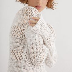 a woman in a white sweater is posing for the camera with her hand on her shoulder