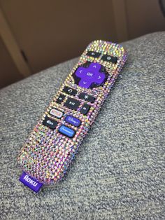 a colorful remote control sitting on top of a gray couch next to a black wall