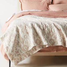 an unmade bed with pink and white linens on the headboard, along with two pillows