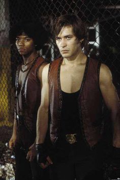 two young men standing next to each other in front of a chain link fence and looking at the camera