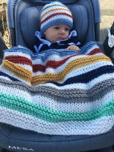 a baby in a stroller with a blanket on it's back, wearing a knitted hat