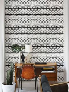 a living room with black and white wallpaper, a chair, desk and potted plant