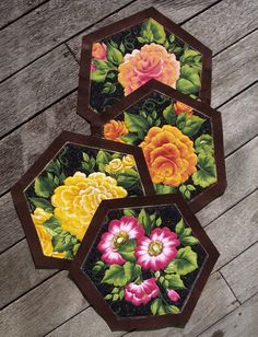 three coasters with flowers painted on them sitting on a wooden floor next to each other
