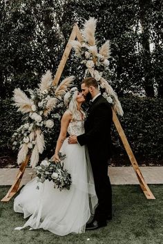 a bride and groom kissing in front of an arch decorated with pamodia flowers