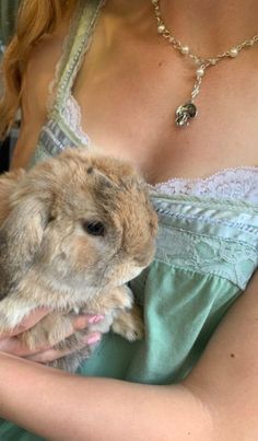 a woman is holding a small rabbit in her arms and wearing a green dress with white lace on it