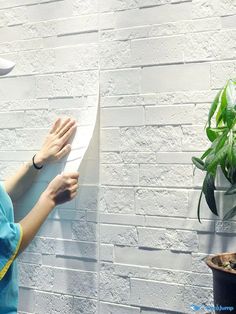 a woman in blue shirt standing next to a white brick wall holding a piece of paper