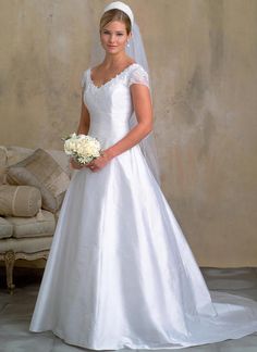 a woman in a white wedding dress standing next to a couch and holding a bouquet