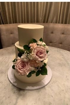 a three tiered wedding cake with pink flowers and greenery sits on a marble table