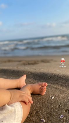 a baby is sitting on the beach with his feet in the sand and looking at the water