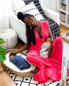 a woman in a red dress sitting on a couch with a baby next to her