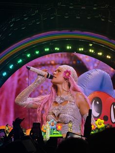 a woman with pink hair singing into a microphone