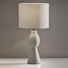 a white table lamp sitting on top of a table next to a light bulb with a beige shade