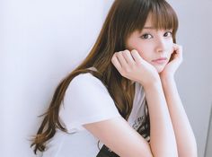 a young woman leaning against a wall with her hand on her chin and looking at the camera