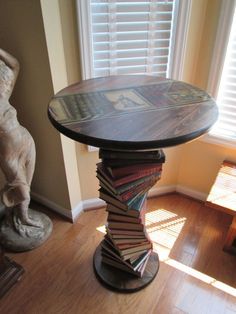 a stack of books sitting on top of a wooden table next to a statue and window