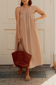 a woman standing in front of a white door holding a brown bag and wearing sandals