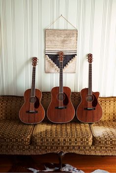 three guitars sitting on top of a couch in front of a wall with a rug