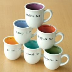 five coffee mugs with different colored tea in them on top of a wooden table