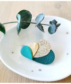 two heart shaped brooches sitting on top of a white plate next to green leaves