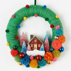 a christmas wreath hanging on the wall with ornaments around it and a house in the background