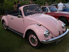 an old pink vw bug is parked in the grass