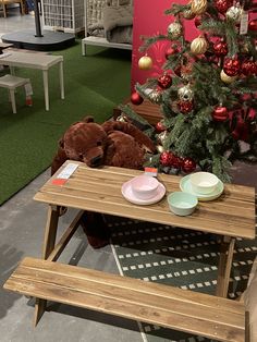 a teddy bear is sitting on a bench next to a table with plates and cups