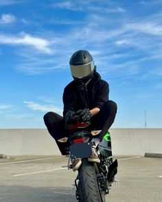 a man riding on the back of a motorcycle in a parking lot next to a cement wall