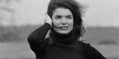 black and white photograph of a woman with her hair in the air, wearing a turtle neck sweater