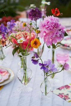 three vases filled with colorful flowers on top of a white tablecloth covered table