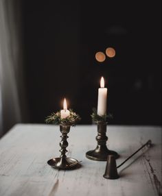 two candles sitting on top of a table next to each other with greenery in them