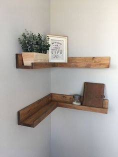 two wooden shelves with plants and books on them in the corner of a white room