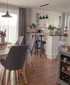 a kitchen and dining room with white cabinets, wood floors and gray chairs in front of the table