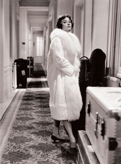 a woman in a fur coat standing next to suitcases on the floor and looking off into the distance