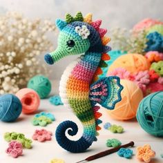 a crocheted seahorse is next to balls of yarn and needles on a table