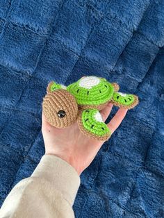 a hand holding a crocheted turtle on top of a blue blanket