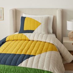 a bed with yellow, blue and green quilted bedspread on top of it