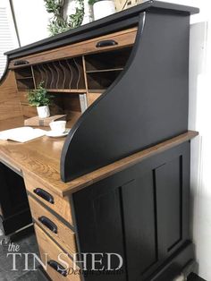 a black and wood desk with drawers on it's sides, next to a potted plant