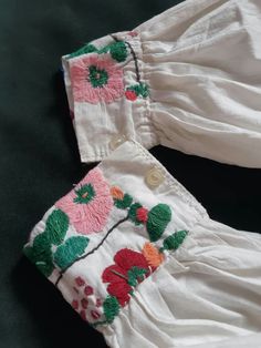 two white pants with flowers on them sitting on top of a black surface, one has pink and green trim