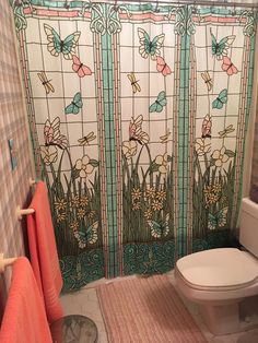 a bathroom with a stained glass shower curtain and toilet in the corner, along with a rug on the floor